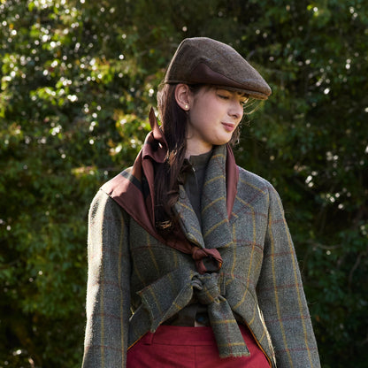 Woman wearing a plaid coat, cap, and Blooms of Autumn silk scarf standing against a green leafy background