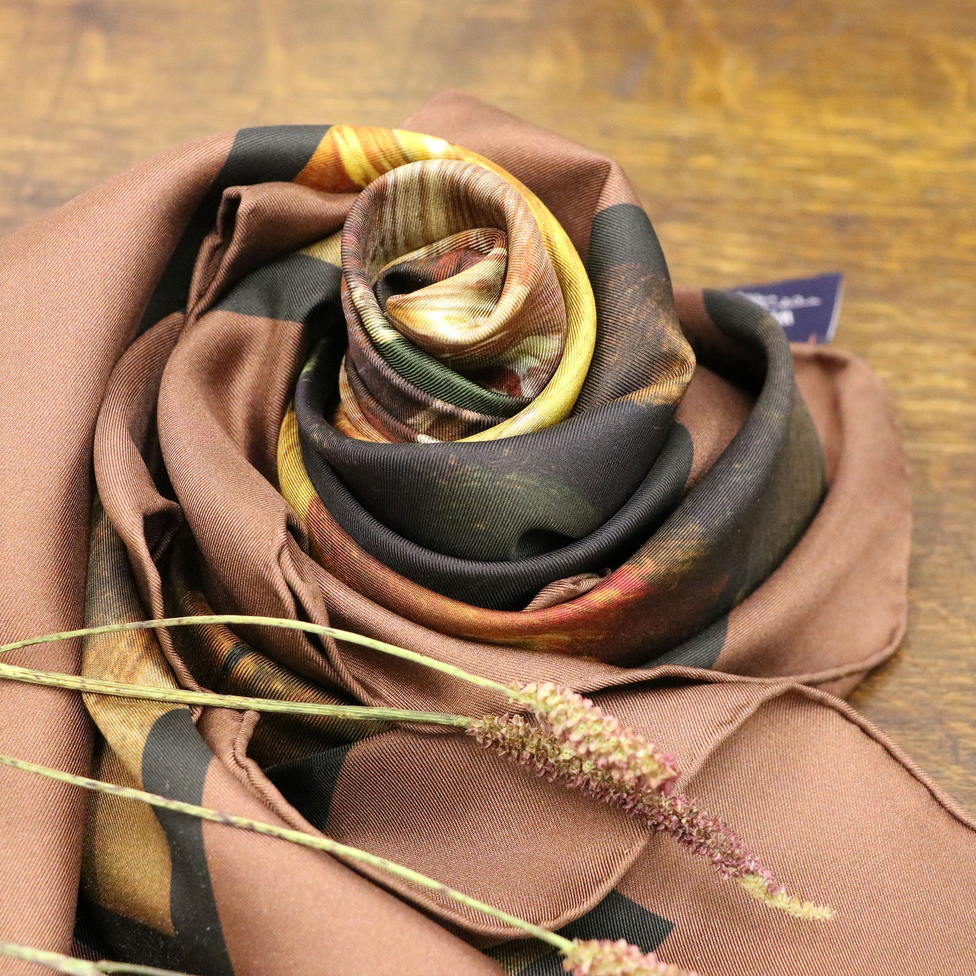 Blooms of Autumn silk scarf wrapped as a rose, shown on wooden table with foliage