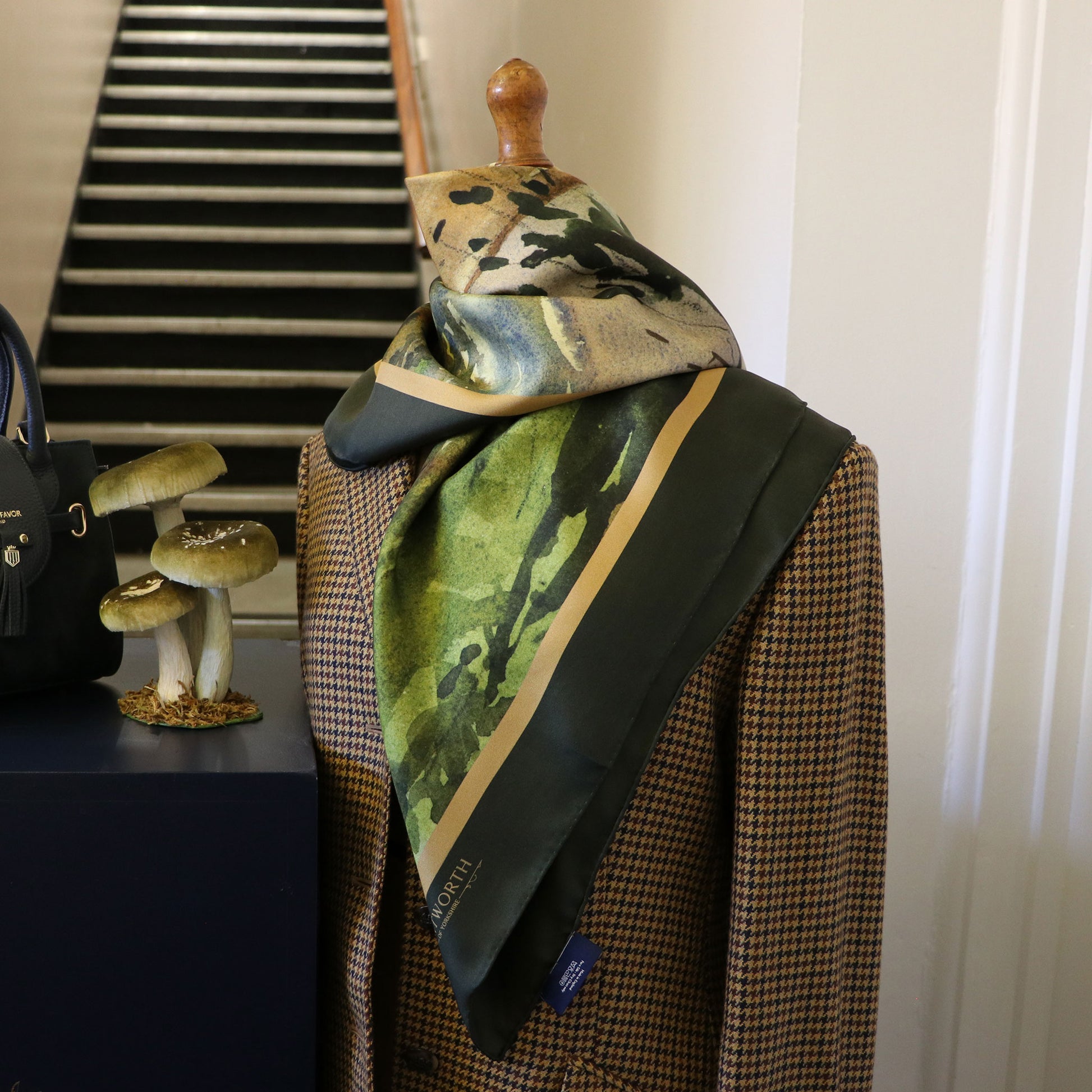 Mannequin wearing tweed jacket with By the Castle Gate silk scarf draped around neck.