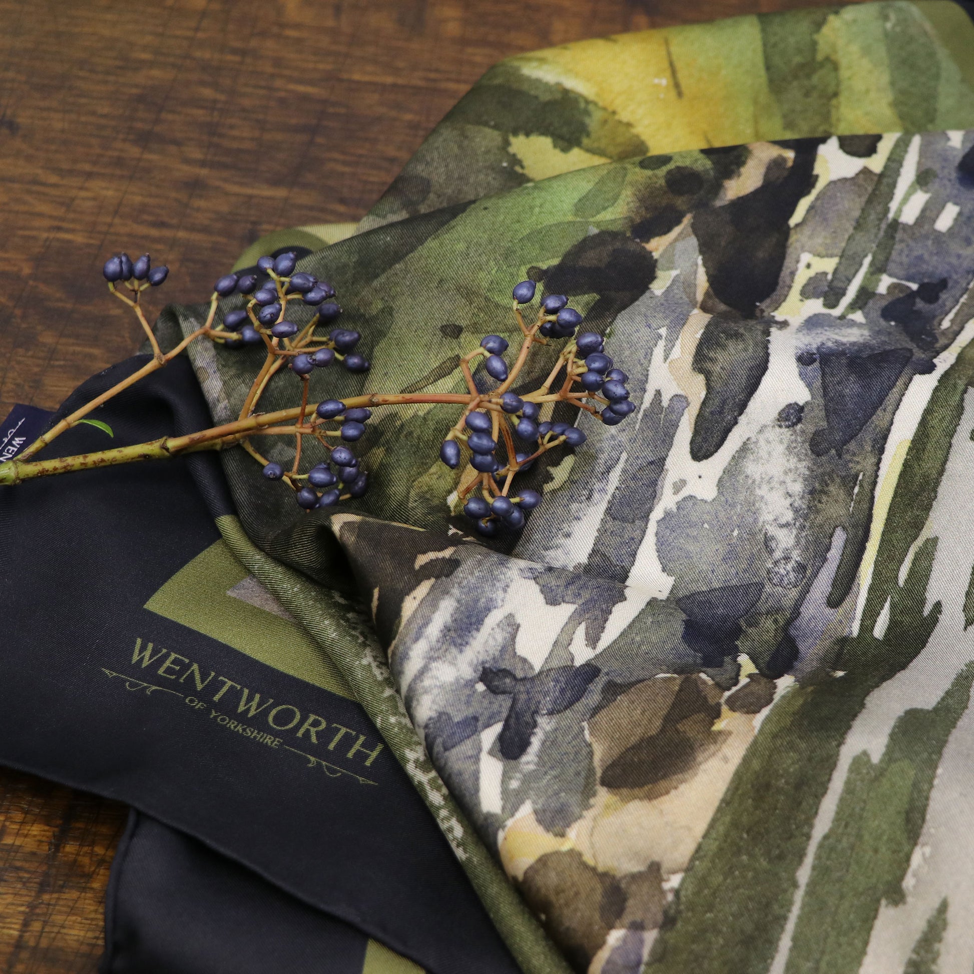 Close up of Where the Salmon Leap silk scarf on table with foliage, showing the Wentworth brand | Silk Scarf | Wentworth of Yorkshire